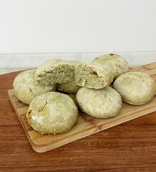 7 Bollitos redondos de pan hecho con salicornia en polvo, bajo en sodio, encima de una tabla de madera.